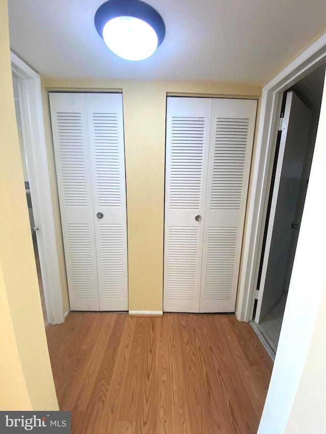 unfurnished bedroom with light wood-type flooring, baseboards, and multiple closets