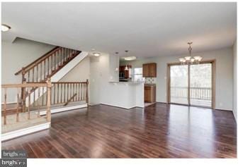 unfurnished living room featuring stairs, an inviting chandelier, and wood finished floors