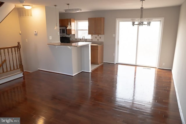 kitchen with decorative light fixtures, stainless steel microwave, a peninsula, and dark wood-style flooring