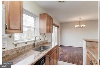 kitchen featuring light stone countertops, decorative light fixtures, a chandelier, dishwashing machine, and a sink