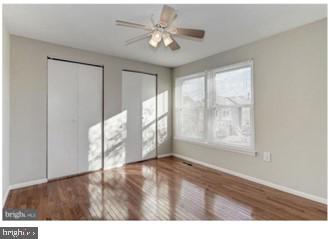 unfurnished bedroom featuring two closets, a ceiling fan, baseboards, and wood finished floors