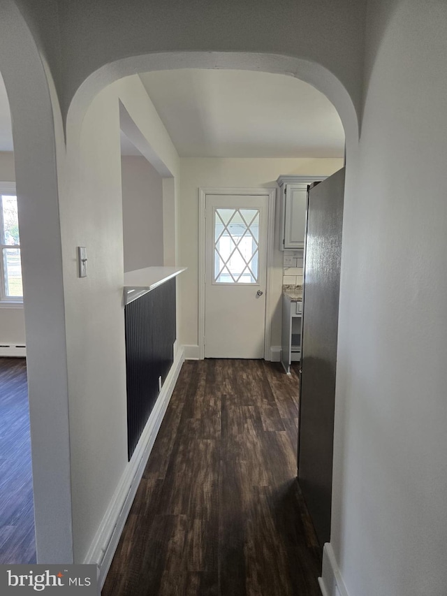 doorway to outside featuring dark wood-style floors, baseboard heating, arched walkways, and baseboards