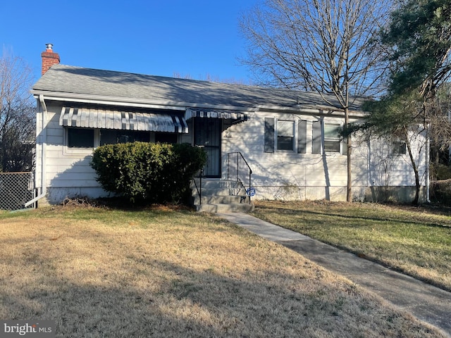 view of front of home with a shingled roof, a chimney, and a front yard