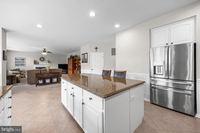 kitchen with light tile patterned floors, a kitchen island, visible vents, dark stone counters, and stainless steel fridge