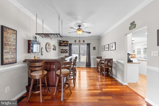 bar with a dry bar, light wood finished floors, visible vents, and ornamental molding