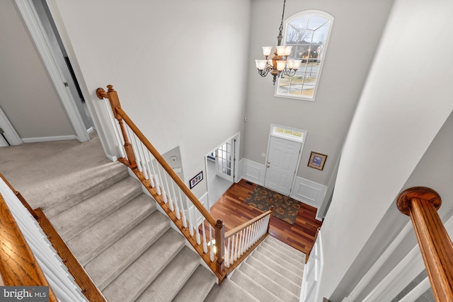 foyer with stairs, wood finished floors, a towering ceiling, and a notable chandelier