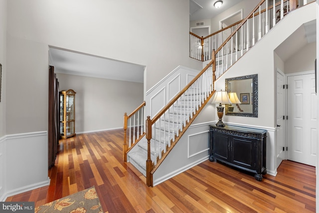 stairs featuring baseboards, a high ceiling, visible vents, and wood finished floors