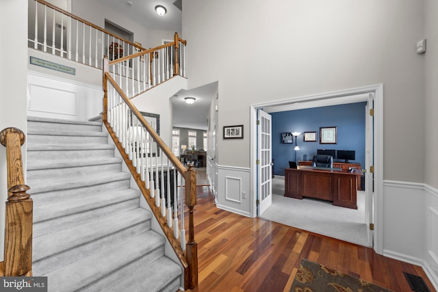 staircase with a towering ceiling, a wainscoted wall, visible vents, and wood finished floors