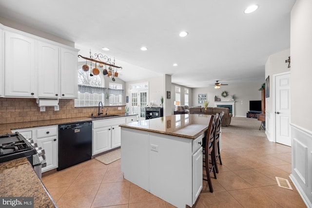 kitchen featuring light tile patterned flooring, a fireplace, a sink, black dishwasher, and a center island