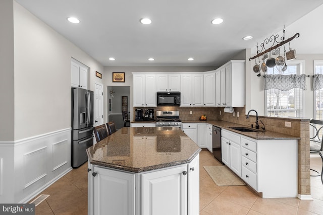 kitchen with wainscoting, a sink, white cabinetry, a peninsula, and black appliances