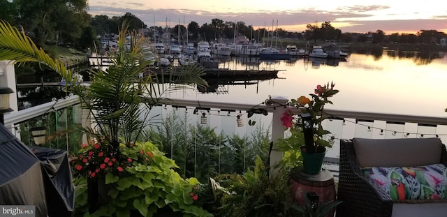 balcony at dusk featuring a dock, a water view, and boat lift