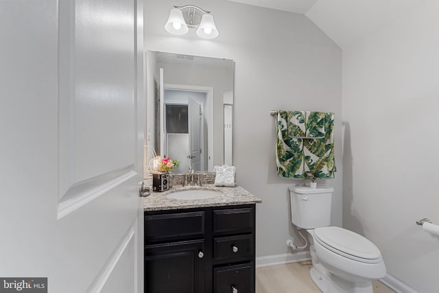 half bathroom with lofted ceiling, toilet, vanity, baseboards, and tile patterned floors