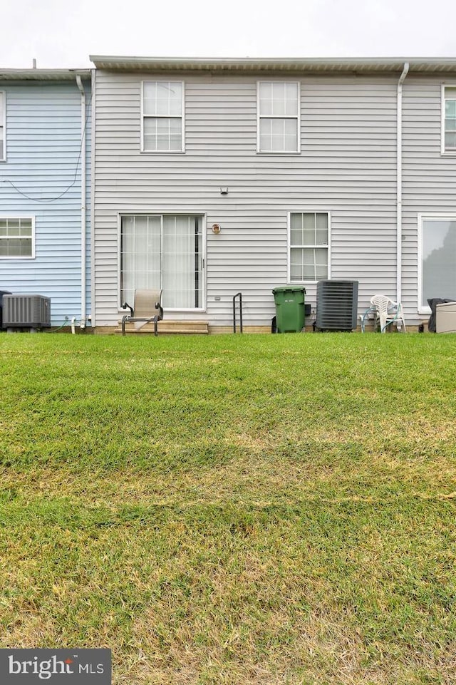 rear view of house featuring central air condition unit and a lawn