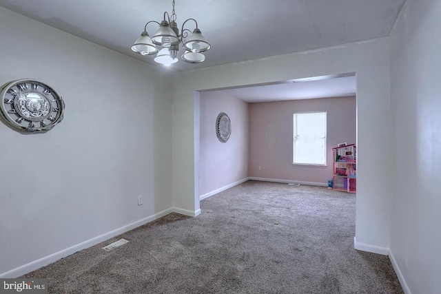 carpeted spare room with visible vents, baseboards, and a notable chandelier