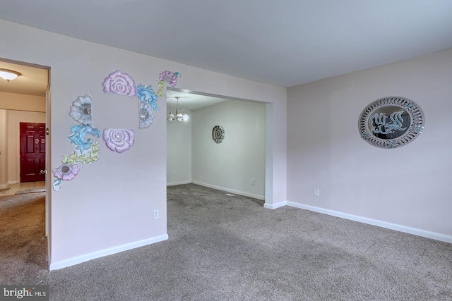 carpeted empty room featuring baseboards and a notable chandelier