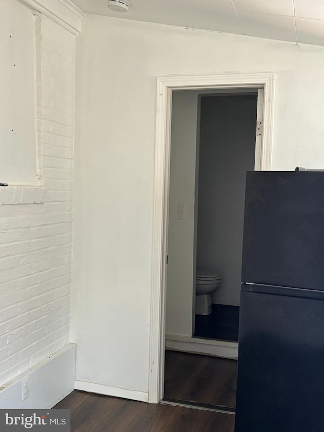 bathroom featuring brick wall, wood finished floors, and toilet