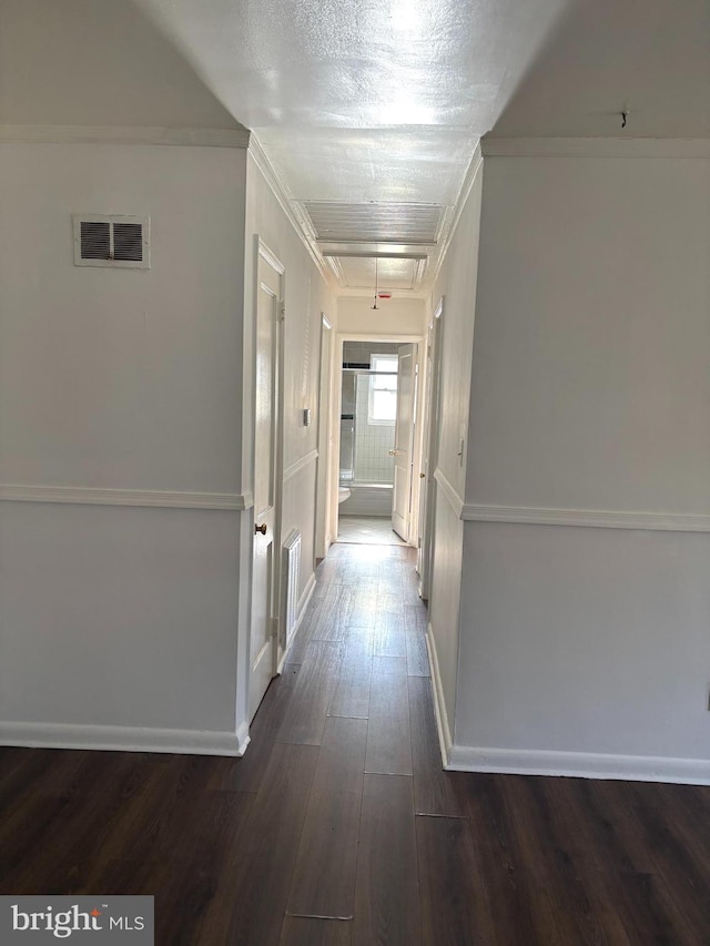 hallway with attic access, crown molding, visible vents, and dark wood-style flooring