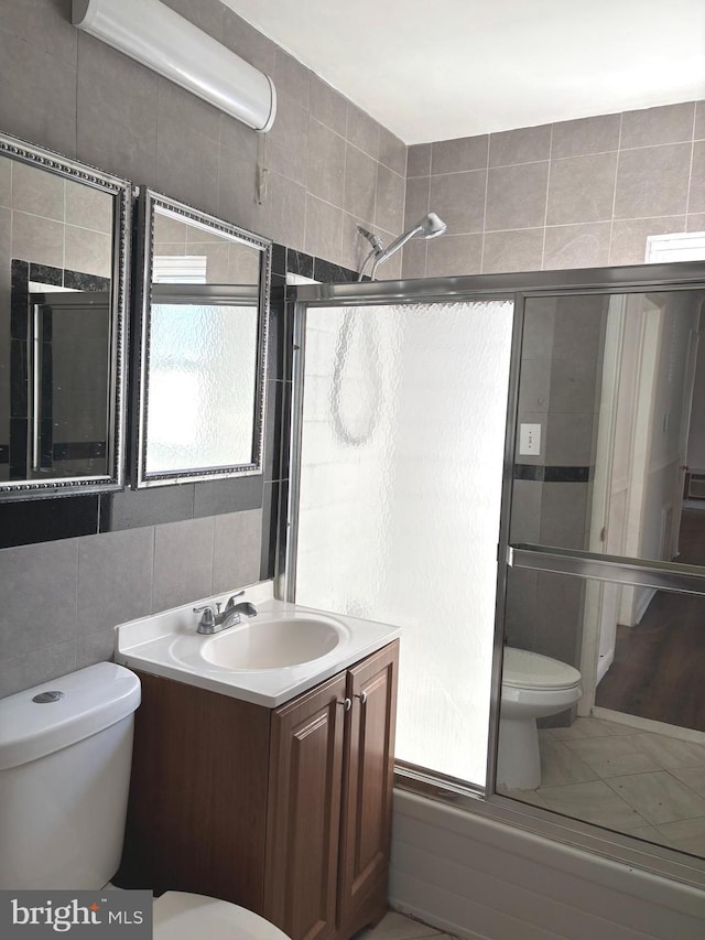 bathroom with toilet, an enclosed shower, tile walls, and vanity