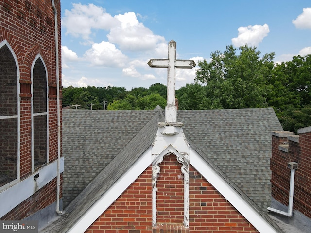 exterior details featuring roof with shingles and brick siding