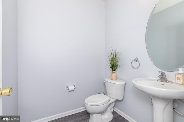 half bath with toilet, wood finished floors, and baseboards