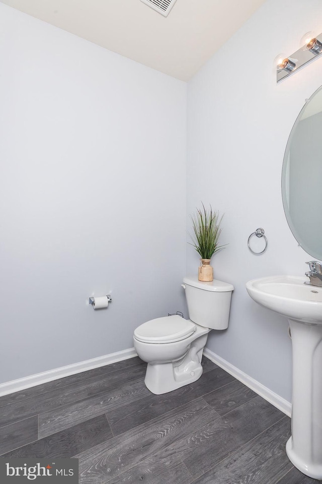 half bath featuring wood finished floors, visible vents, baseboards, a sink, and toilet