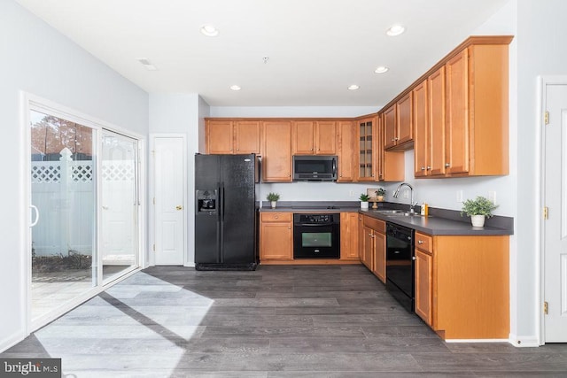 kitchen with dark countertops, glass insert cabinets, dark wood-style floors, black appliances, and a sink