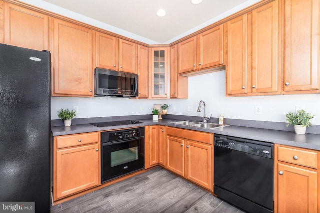 kitchen with dark countertops, glass insert cabinets, wood finished floors, black appliances, and a sink