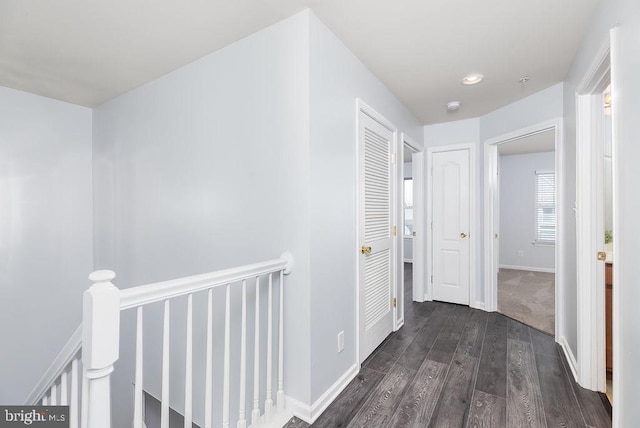 hallway with baseboards, an upstairs landing, and dark wood finished floors