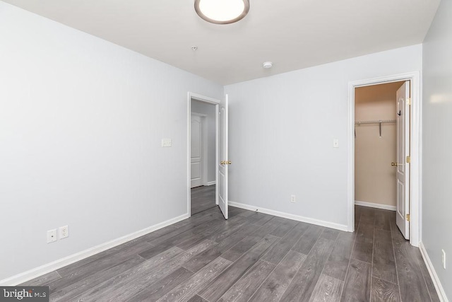 unfurnished bedroom featuring a spacious closet, wood finished floors, baseboards, and a closet