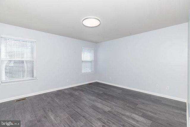 empty room featuring visible vents, baseboards, and dark wood finished floors