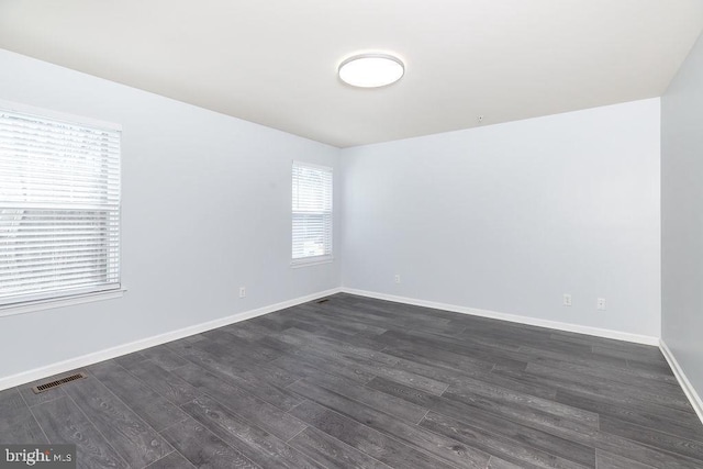 unfurnished room featuring visible vents, baseboards, and dark wood finished floors