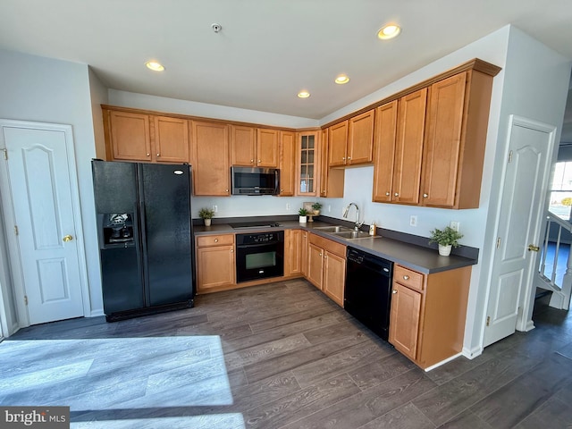 kitchen featuring dark wood-style floors, a sink, black appliances, glass insert cabinets, and dark countertops