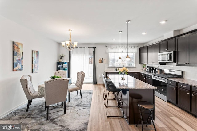 kitchen with appliances with stainless steel finishes, light stone countertops, light wood-type flooring, a chandelier, and backsplash