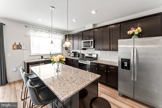 kitchen featuring light stone counters, a breakfast bar area, light wood finished floors, backsplash, and appliances with stainless steel finishes