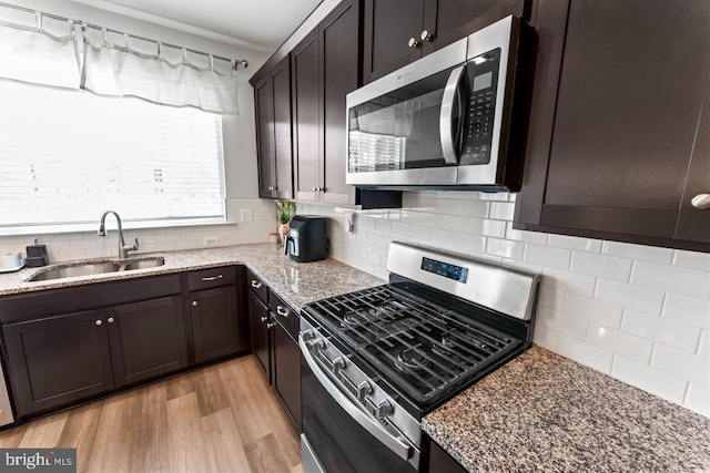 kitchen with light wood finished floors, tasteful backsplash, light stone counters, stainless steel appliances, and a sink