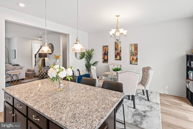 kitchen with light wood finished floors, a kitchen breakfast bar, hanging light fixtures, light stone countertops, and an inviting chandelier