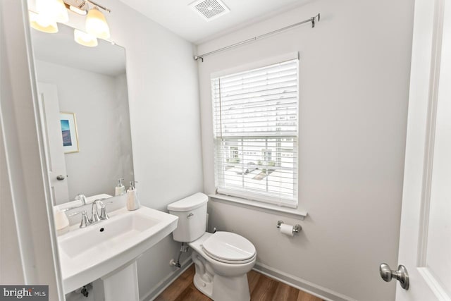 half bath with baseboards, visible vents, toilet, wood finished floors, and a sink