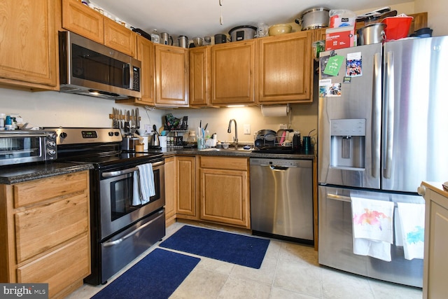 kitchen featuring dark countertops, a toaster, light tile patterned floors, appliances with stainless steel finishes, and a sink