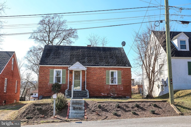 cape cod house featuring a shingled roof and brick siding