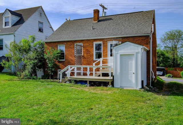 rear view of property featuring a chimney, roof with shingles, a deck, brick siding, and a yard