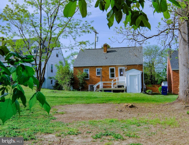 rear view of house with a chimney, roof with shingles, central AC unit, brick siding, and a yard