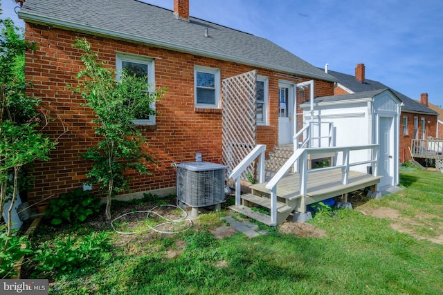 rear view of property with a chimney, a storage shed, central AC unit, brick siding, and an outdoor structure