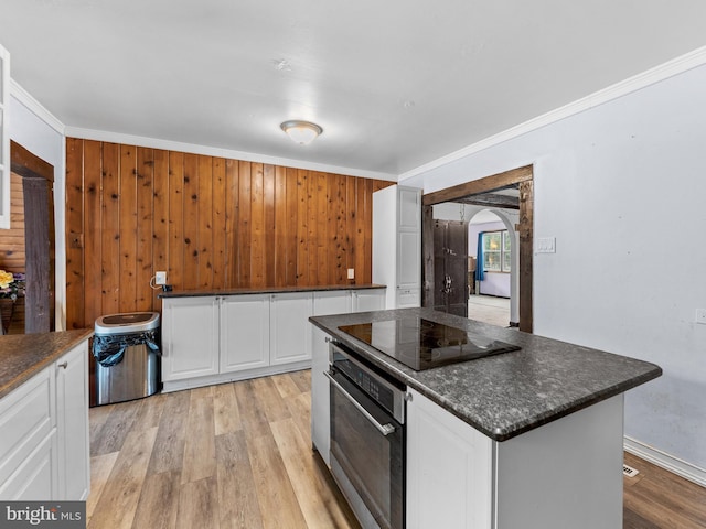 kitchen featuring oven, arched walkways, light wood-style floors, white cabinets, and black electric cooktop