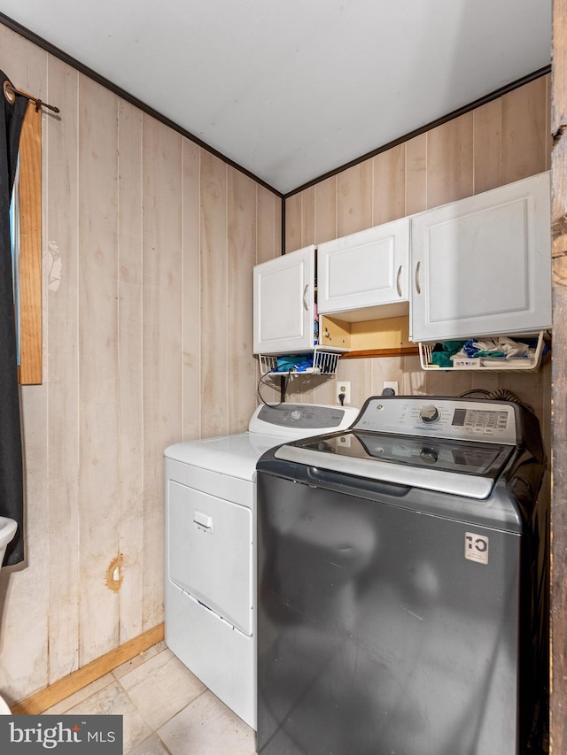 clothes washing area featuring cabinet space, wood walls, and separate washer and dryer