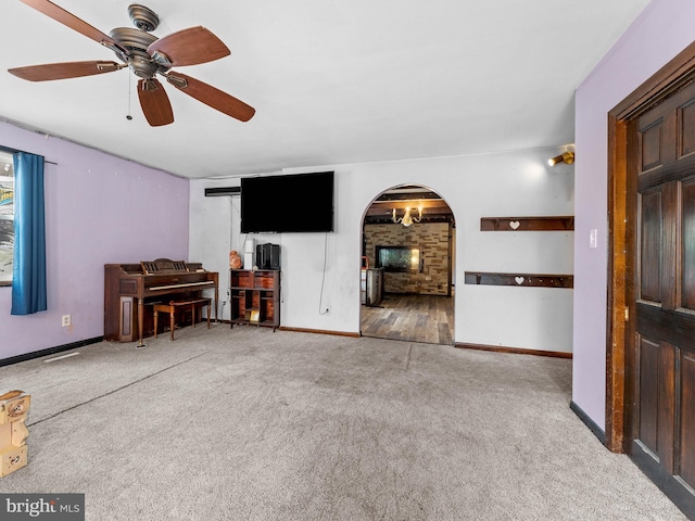 unfurnished living room with arched walkways, baseboards, carpet, and a ceiling fan