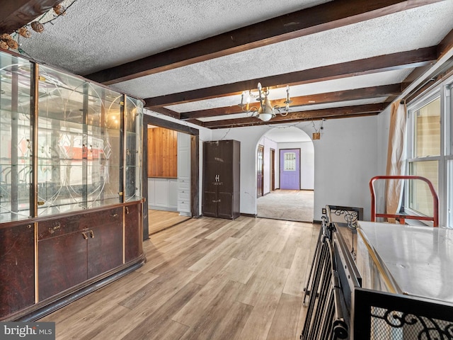 interior space featuring arched walkways, beam ceiling, light wood-style flooring, and a textured ceiling