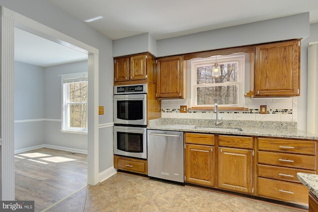 kitchen with backsplash, appliances with stainless steel finishes, light stone countertops, and a sink