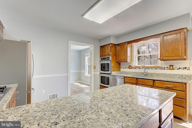 kitchen with visible vents, a sink, appliances with stainless steel finishes, decorative backsplash, and light stone countertops