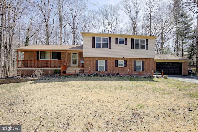 tri-level home with driveway, covered porch, a front yard, an attached garage, and brick siding