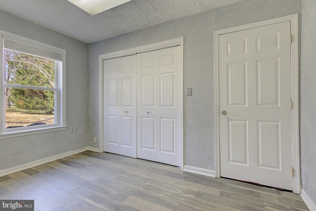 unfurnished bedroom featuring light wood-style flooring, baseboards, a closet, and a textured ceiling